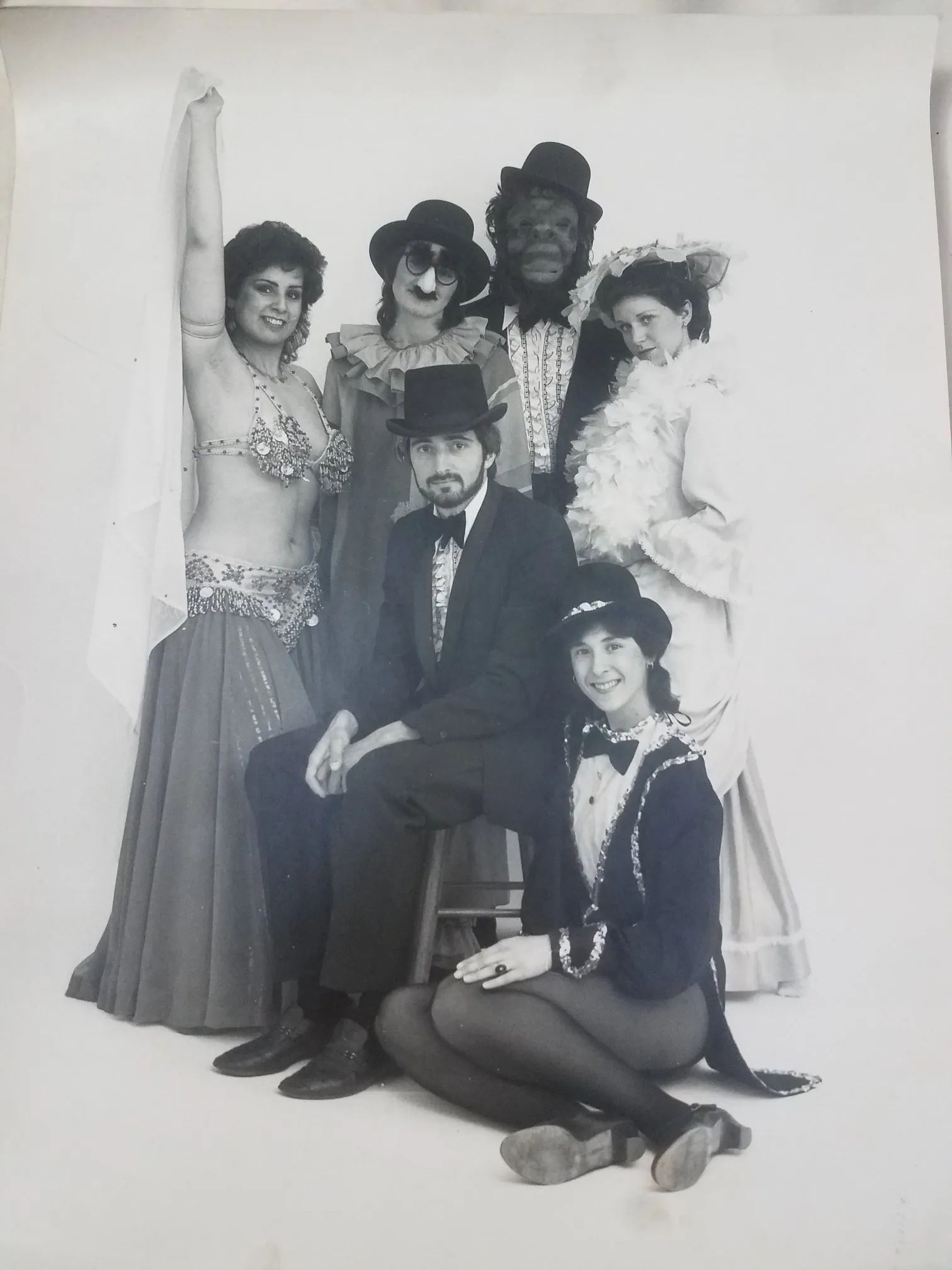 Costume group portrait with a seated man, standing women, and a kneeling woman against a plain backdrop