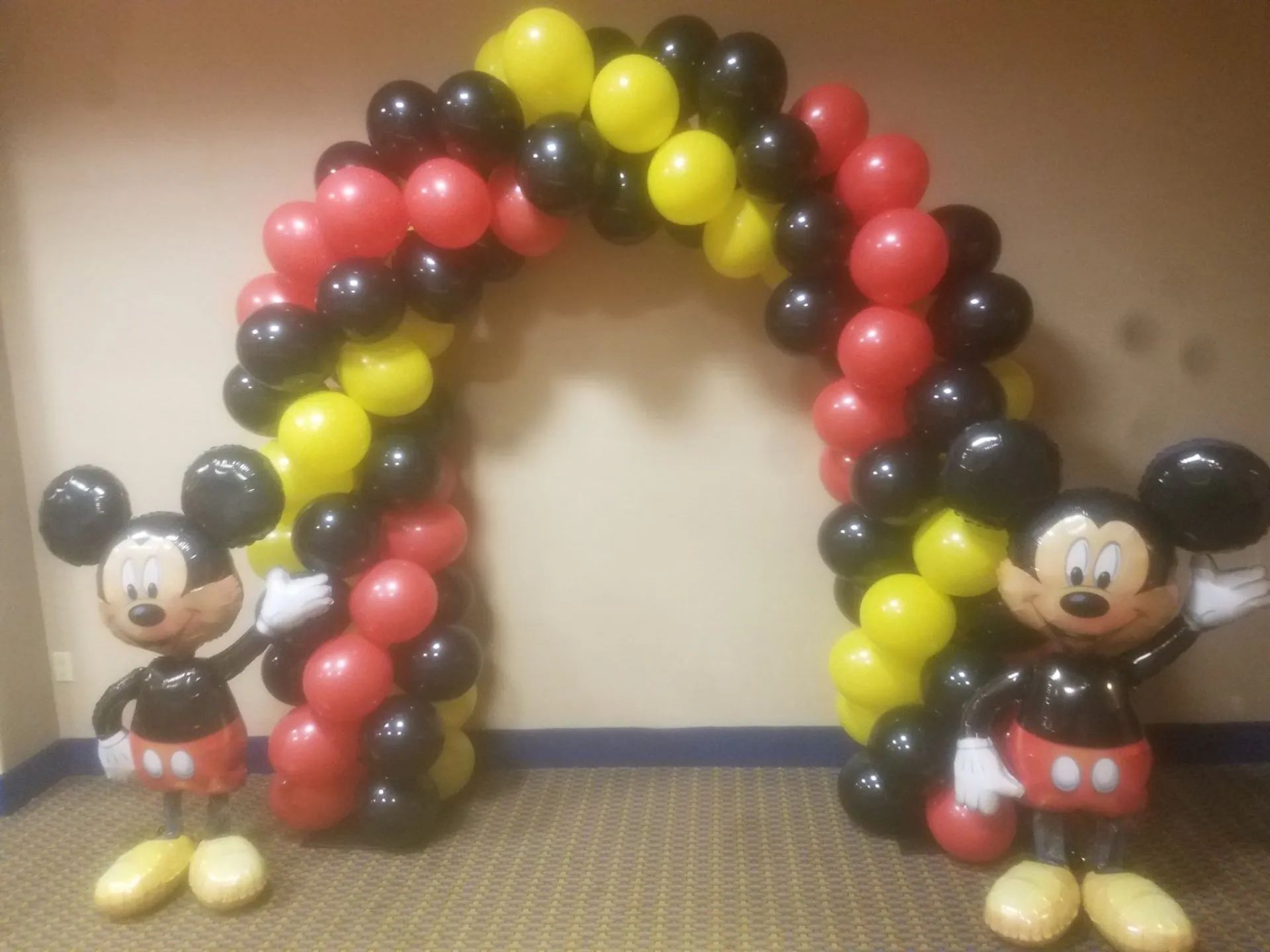 Mickey Mouse balloon figures with a colorful balloon arch on a carpeted floor