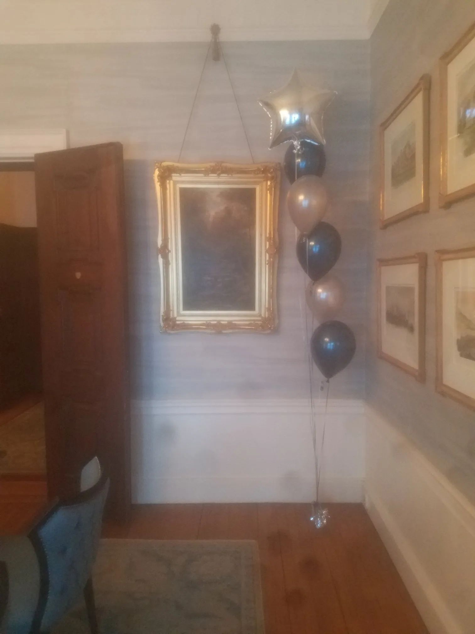 Dining room with framed mirror, balloon bouquet, and framed wall art on light gray walls.