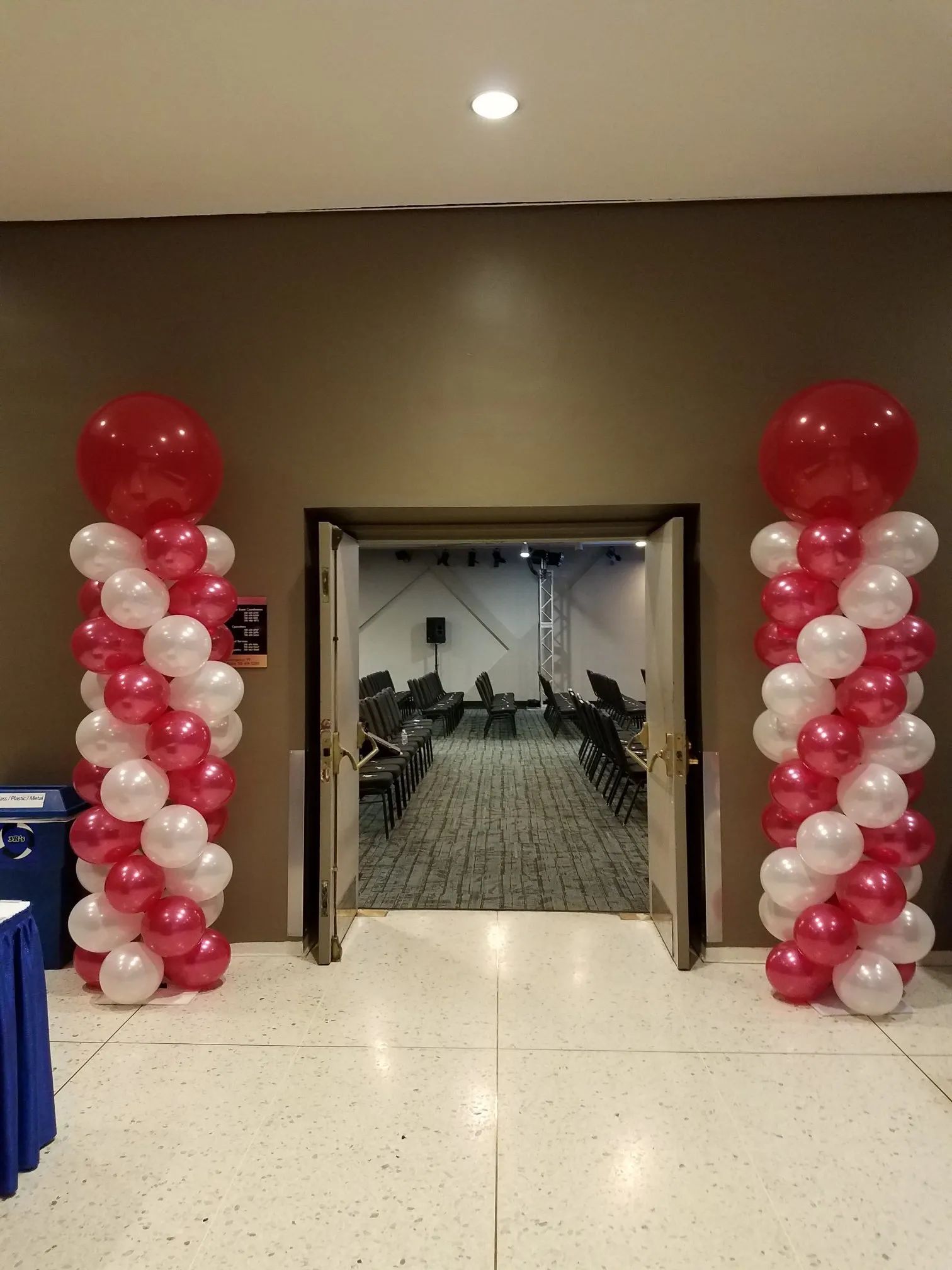 Red-and-white balloon columns flank an open doorway to a room with chairs inside.