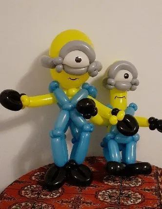 Two balloon animal figures in yellow, blue, and gray on a patterned surface against a plain wall.