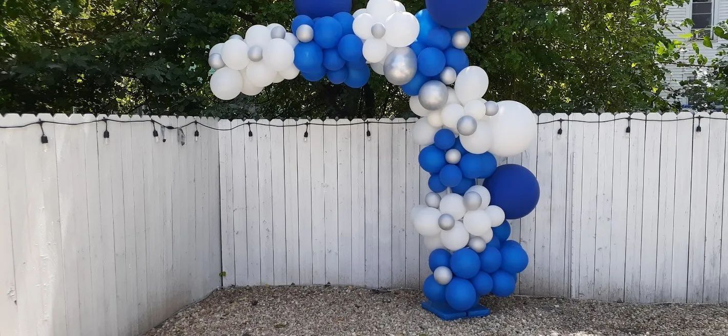 Blue and white balloon arch over a backyard fence and gravel patio