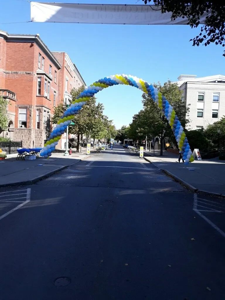 Street arch of blue, yellow, and white balloons over a city road between brick buildings.