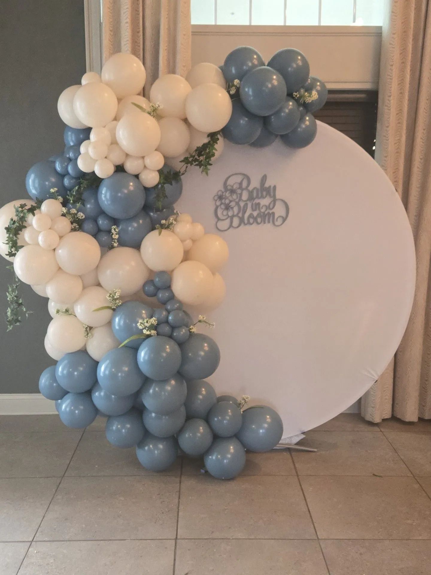 Blue and white balloon arch beside a round sign with “Baby” text at an indoor celebration