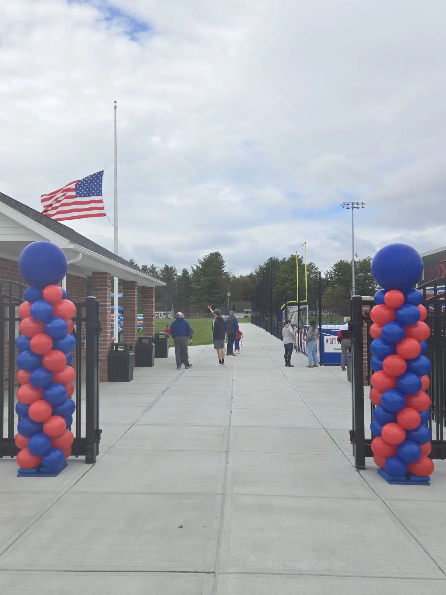 Decorated walkway with red and blue balloon columns, American flag, and people walking toward a building