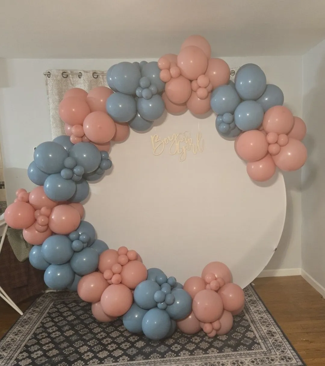 Pastel pink and blue balloon garland framing a white circular backdrop on a patterned rug