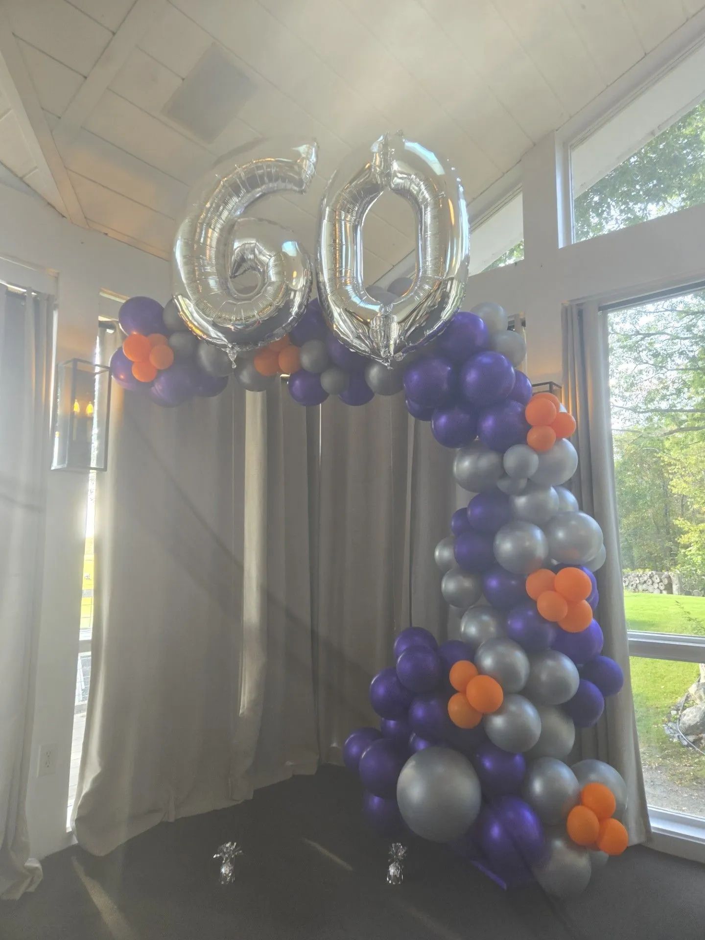 Silver “60” balloons above a purple, blue, and orange balloon arch in a bright indoor space.