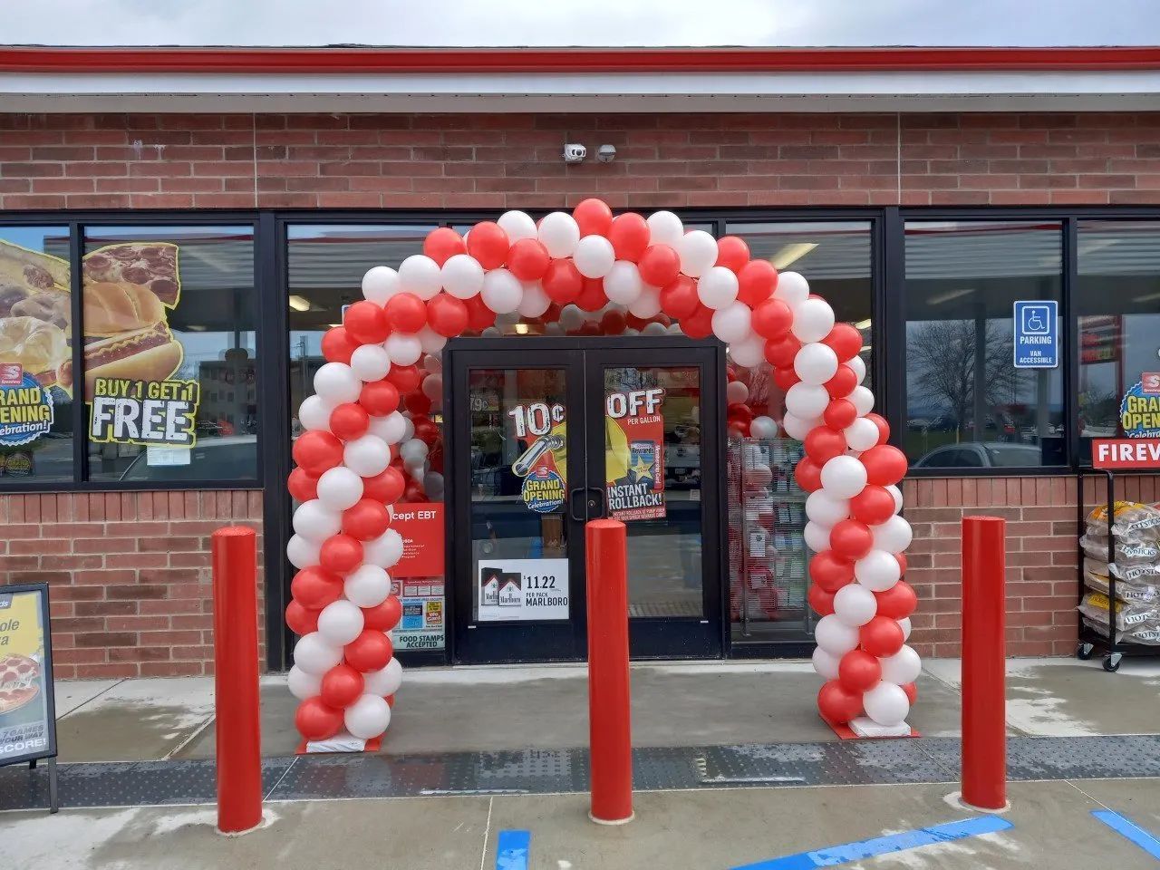 Red and white balloon arch framing a store entrance with red bollards in front
