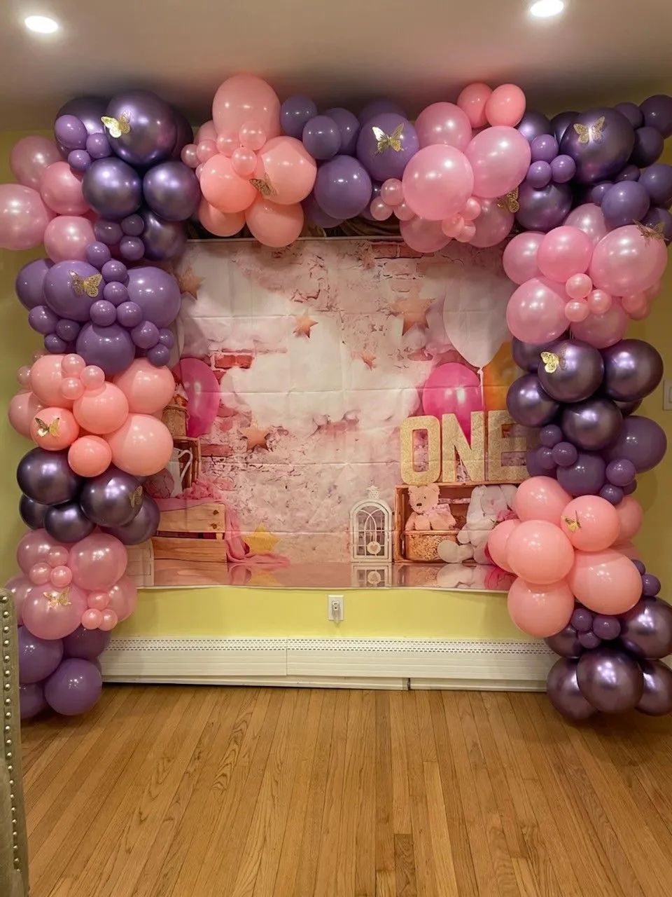 Purple and pink balloon arch framing a decorated party backdrop on a wooden floor