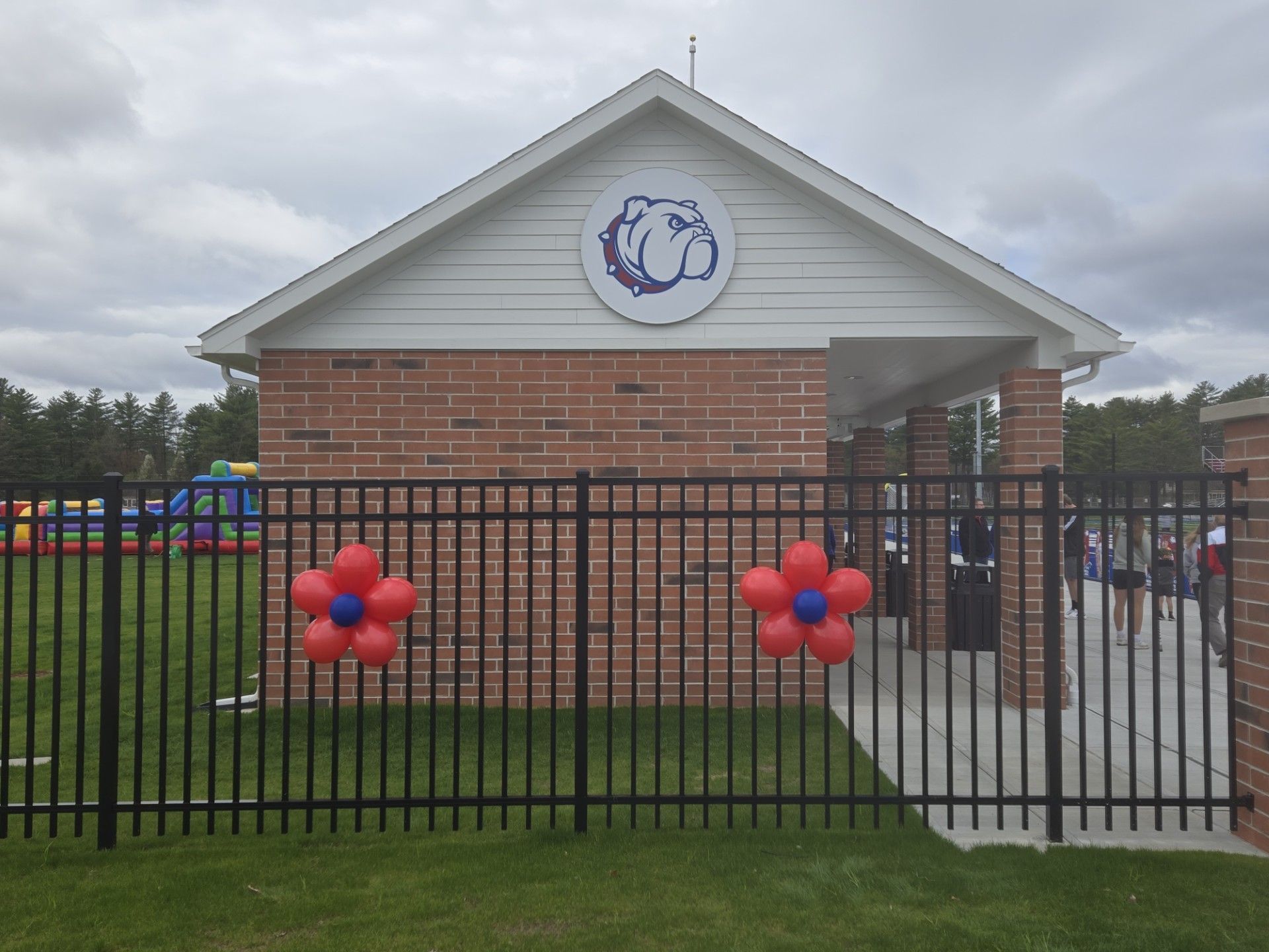 Brick building with school logo behind a black fence, decorated with red balloon flowers.