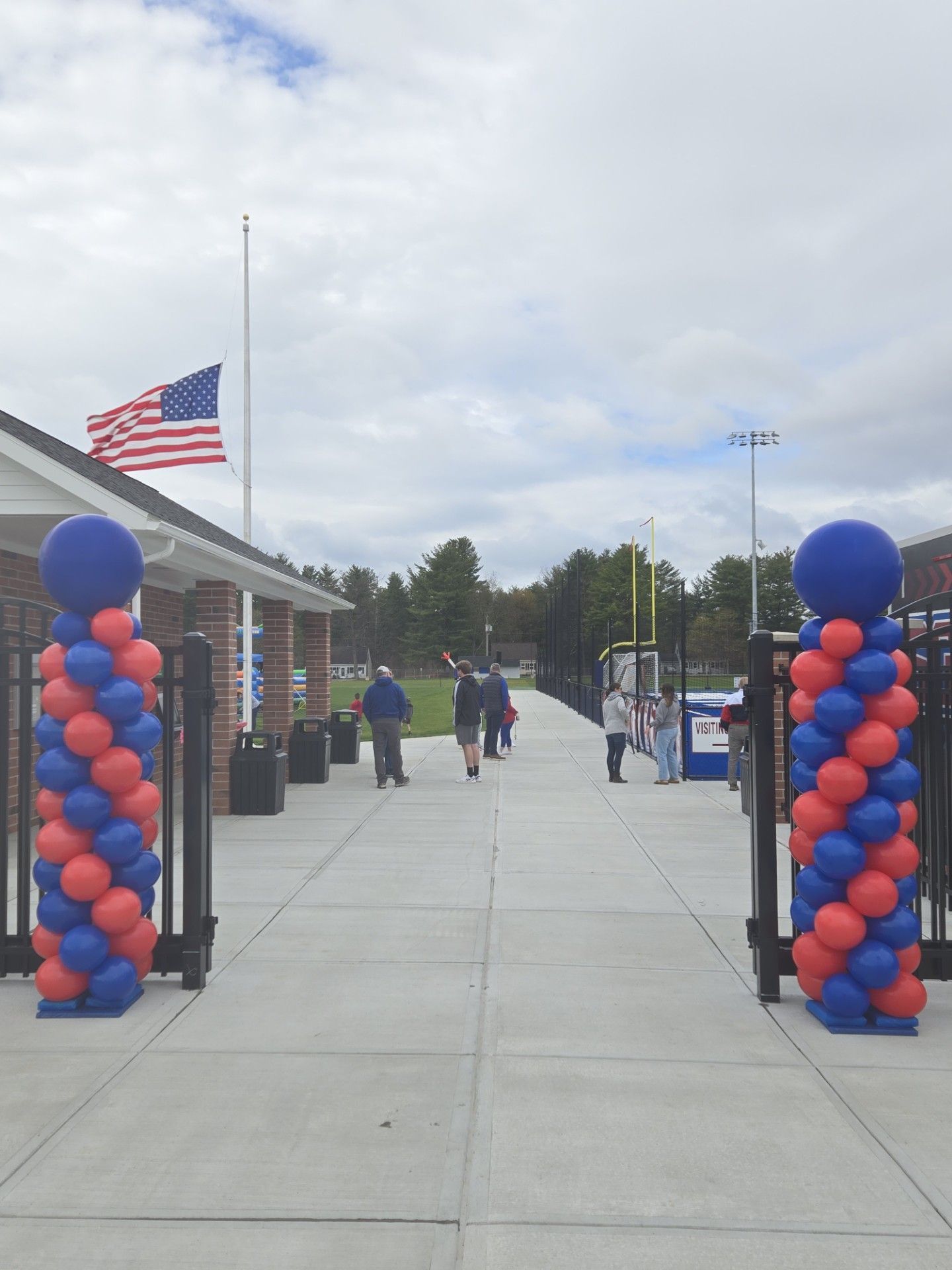 Decorated outdoor walkway with blue and red balloon columns and an American flag on a cloudy day