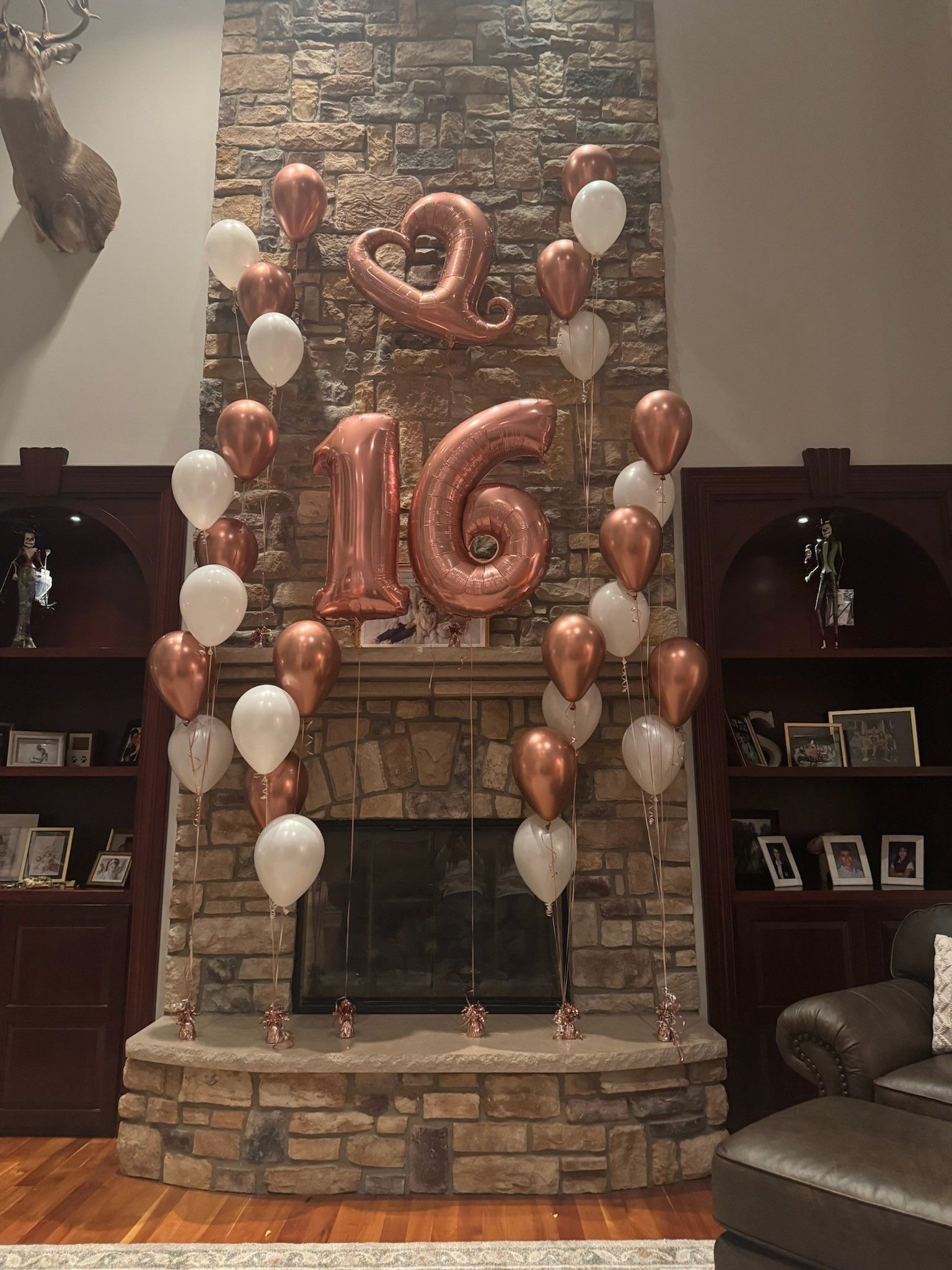 Copper “16” balloons and white balloons decorate a stone fireplace mantel.
