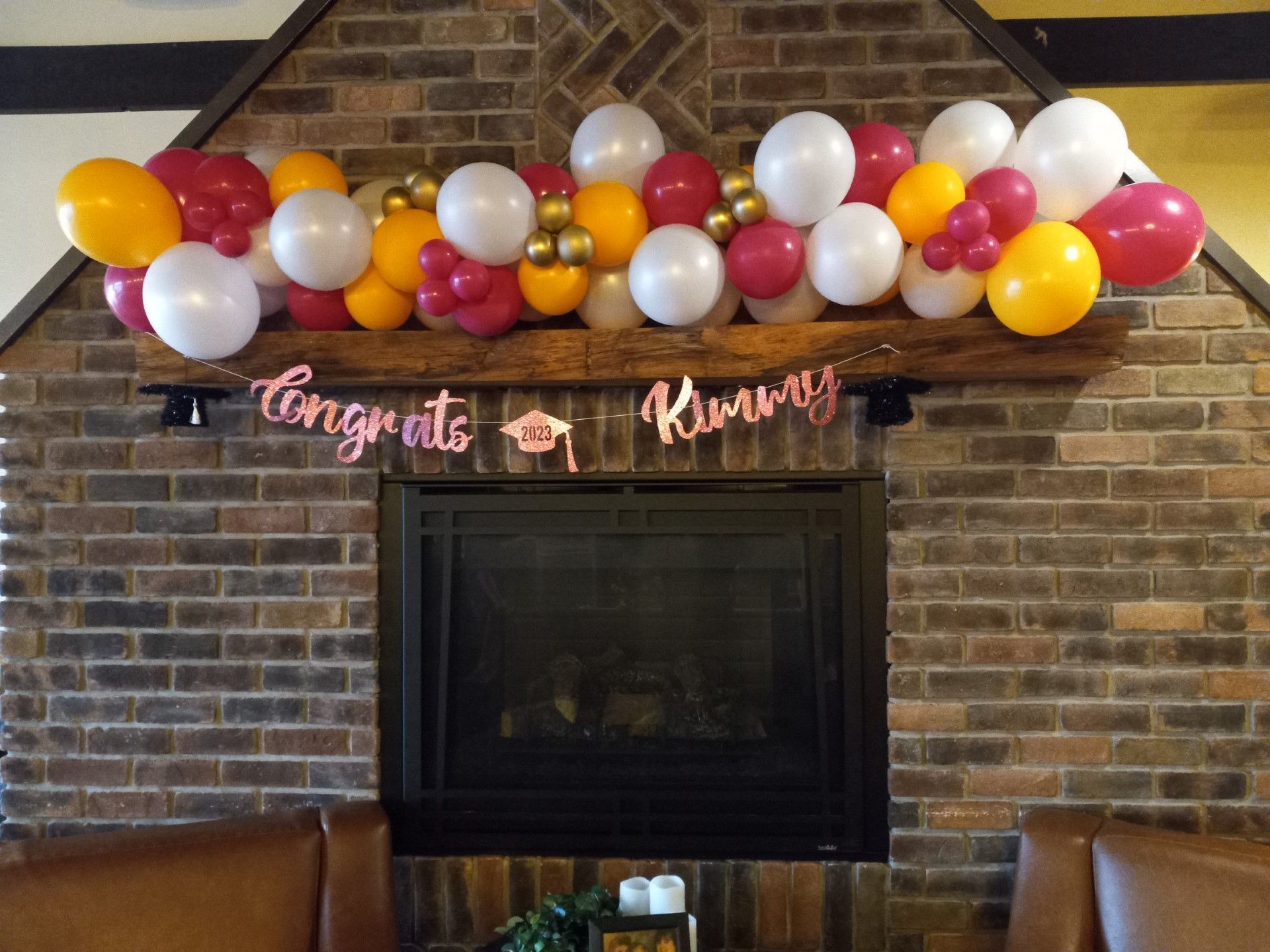 Balloon garland in red, gold, white, and pink above a fireplace with a pink “Congrats Kimberly!” banner.