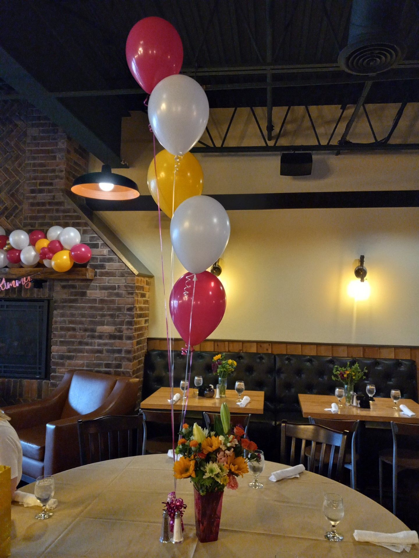 Restaurant table with red, white, and gold balloons and a flower centerpiece in a cozy dining room