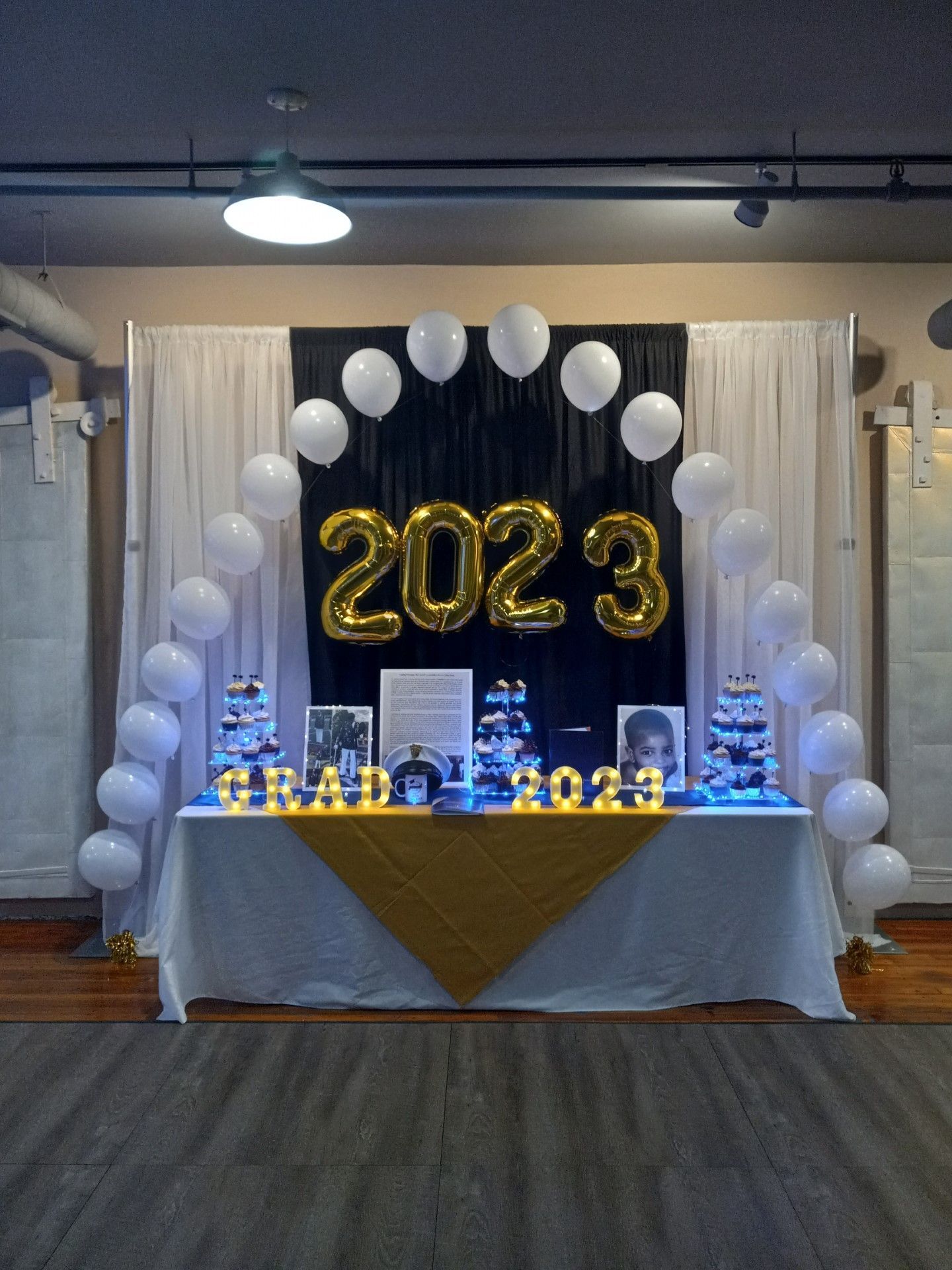 Decorated 2023 celebration table with gold balloons and white balloon arch in an indoor venue