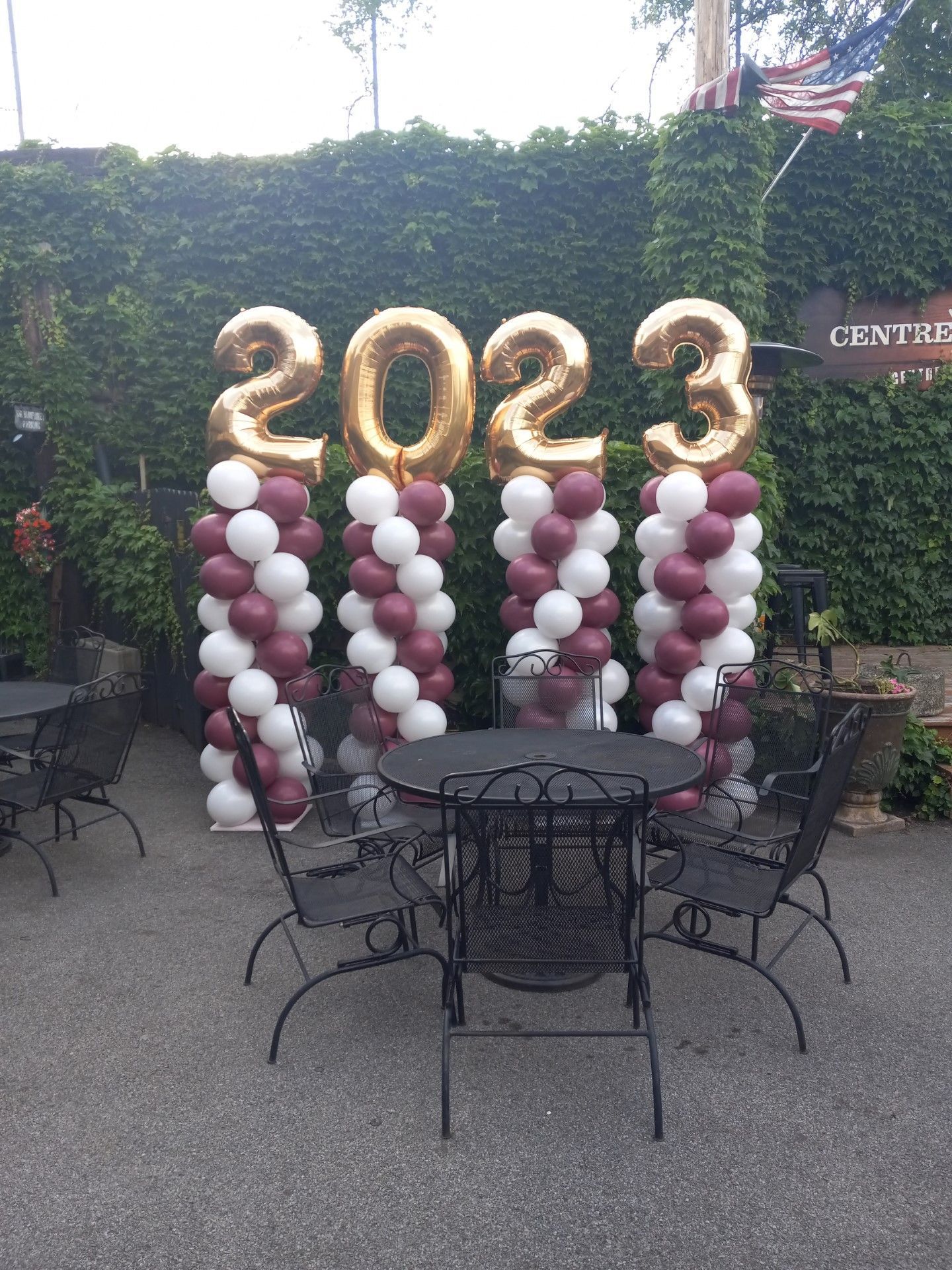 2023 balloon display in white, burgundy, and gold at an outdoor patio with tables and chairs