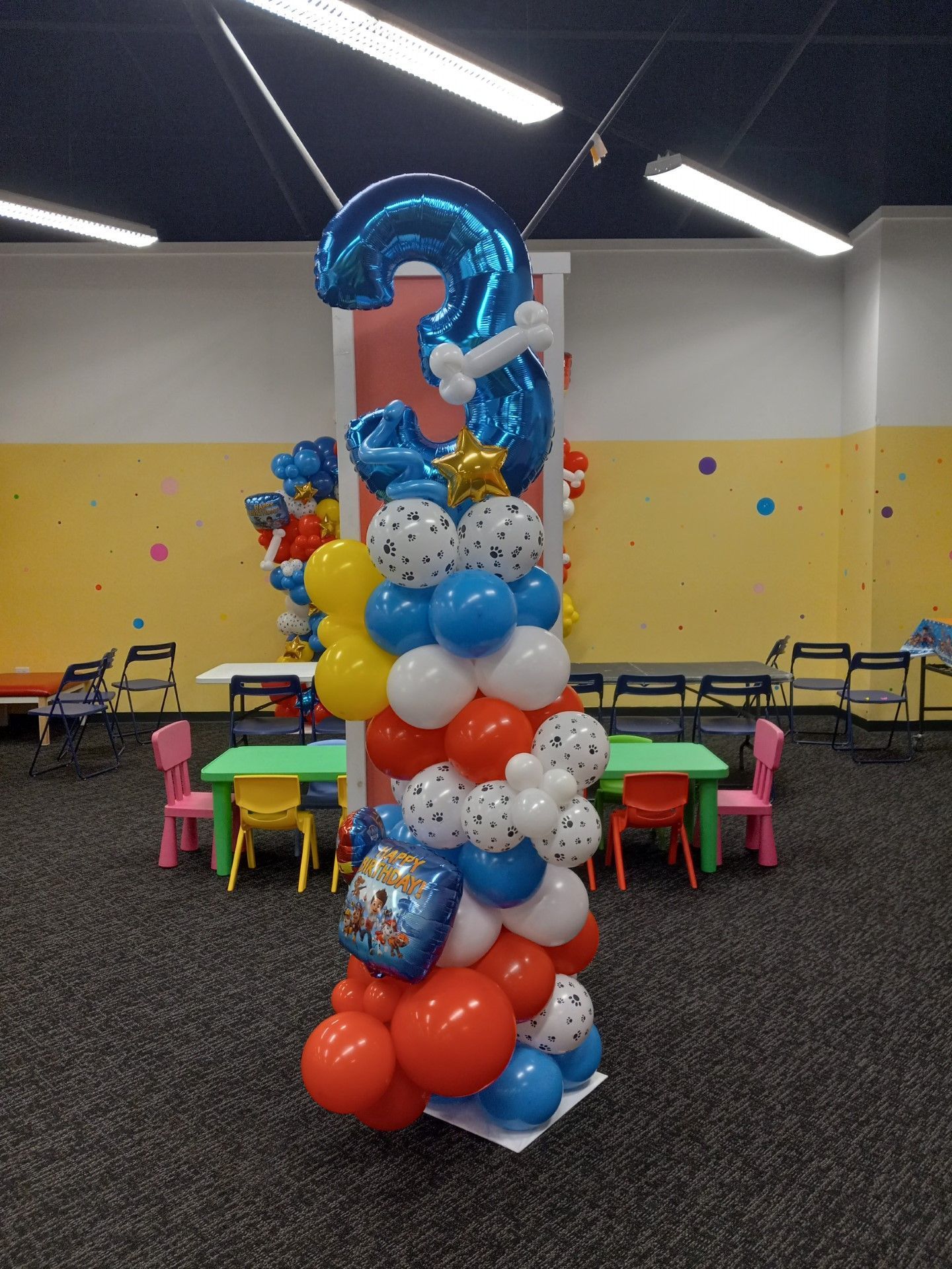 Colorful balloon tower centerpiece in a party room with tables and chairs