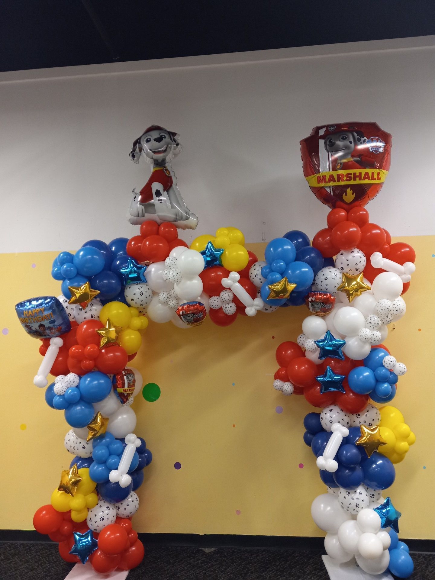 Balloon arch in red, white, blue, and yellow with a Marshall Paw Patrol balloon topper