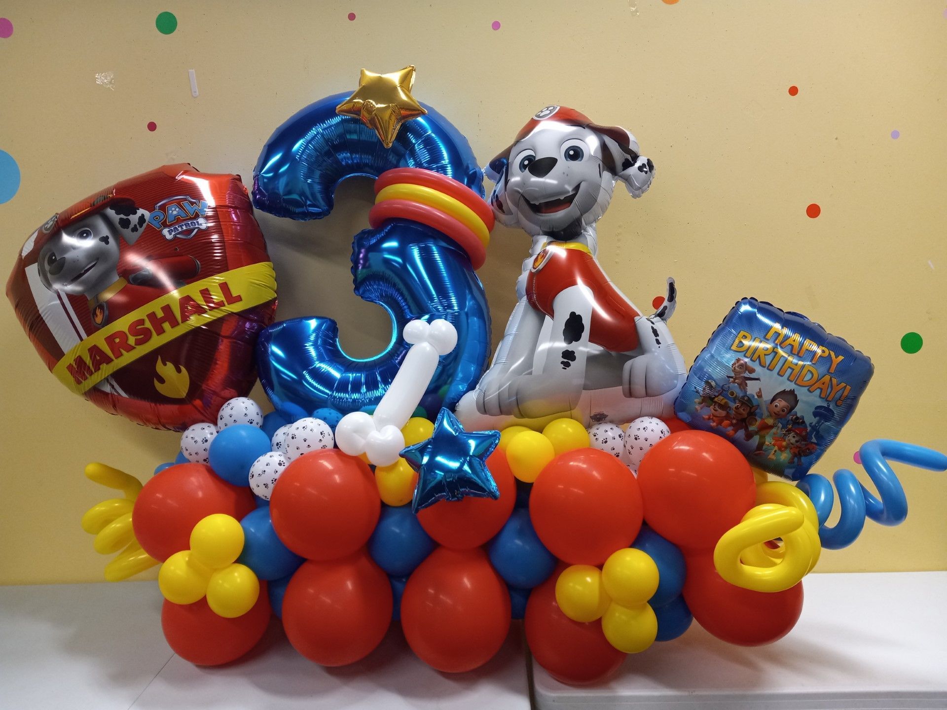 Dog balloon sculpture on a table, with colorful balloon flowers and a blue-and-yellow number 3 display