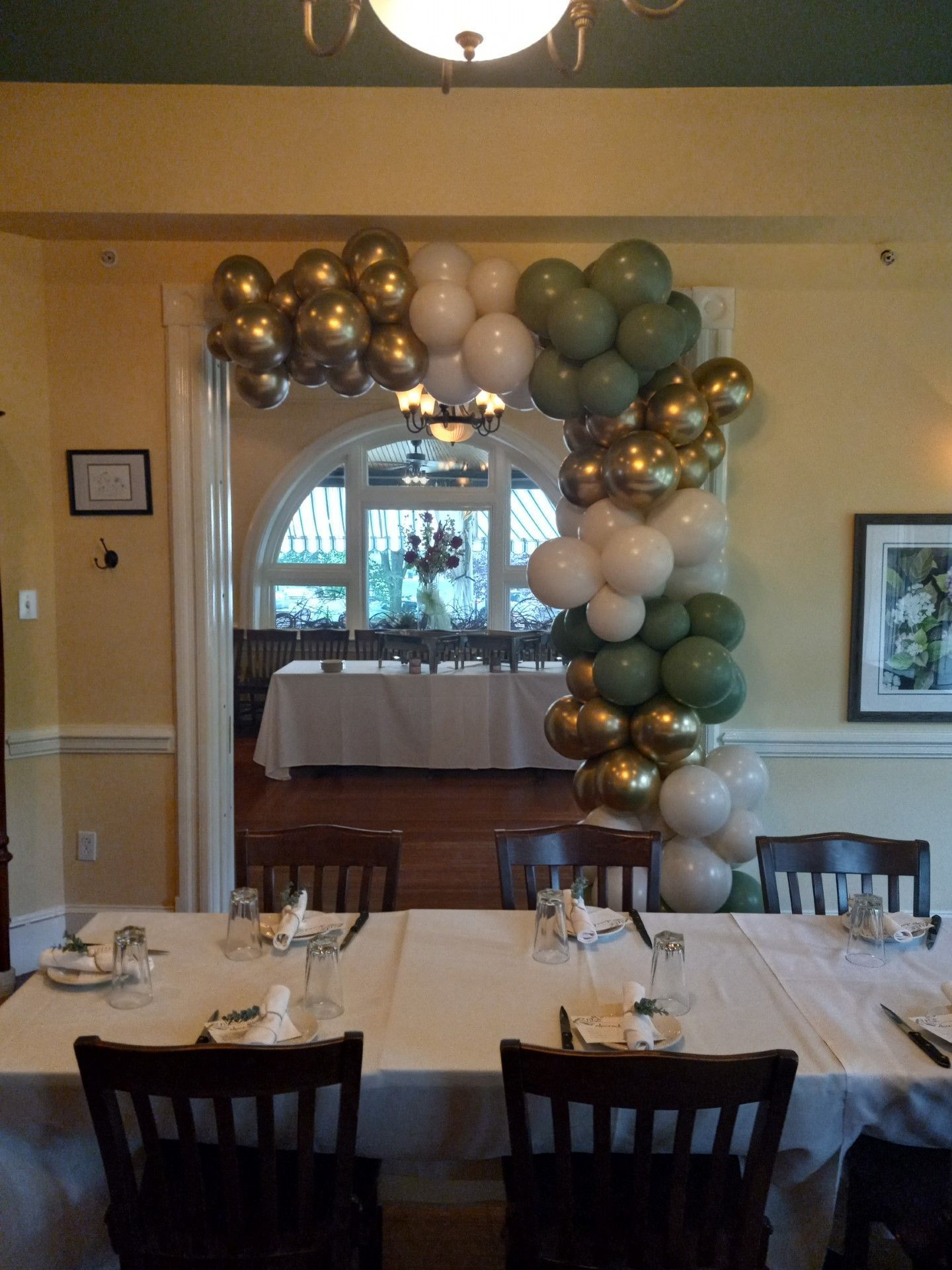 Balloon arch in a banquet room, with white-draped tables set for an event.