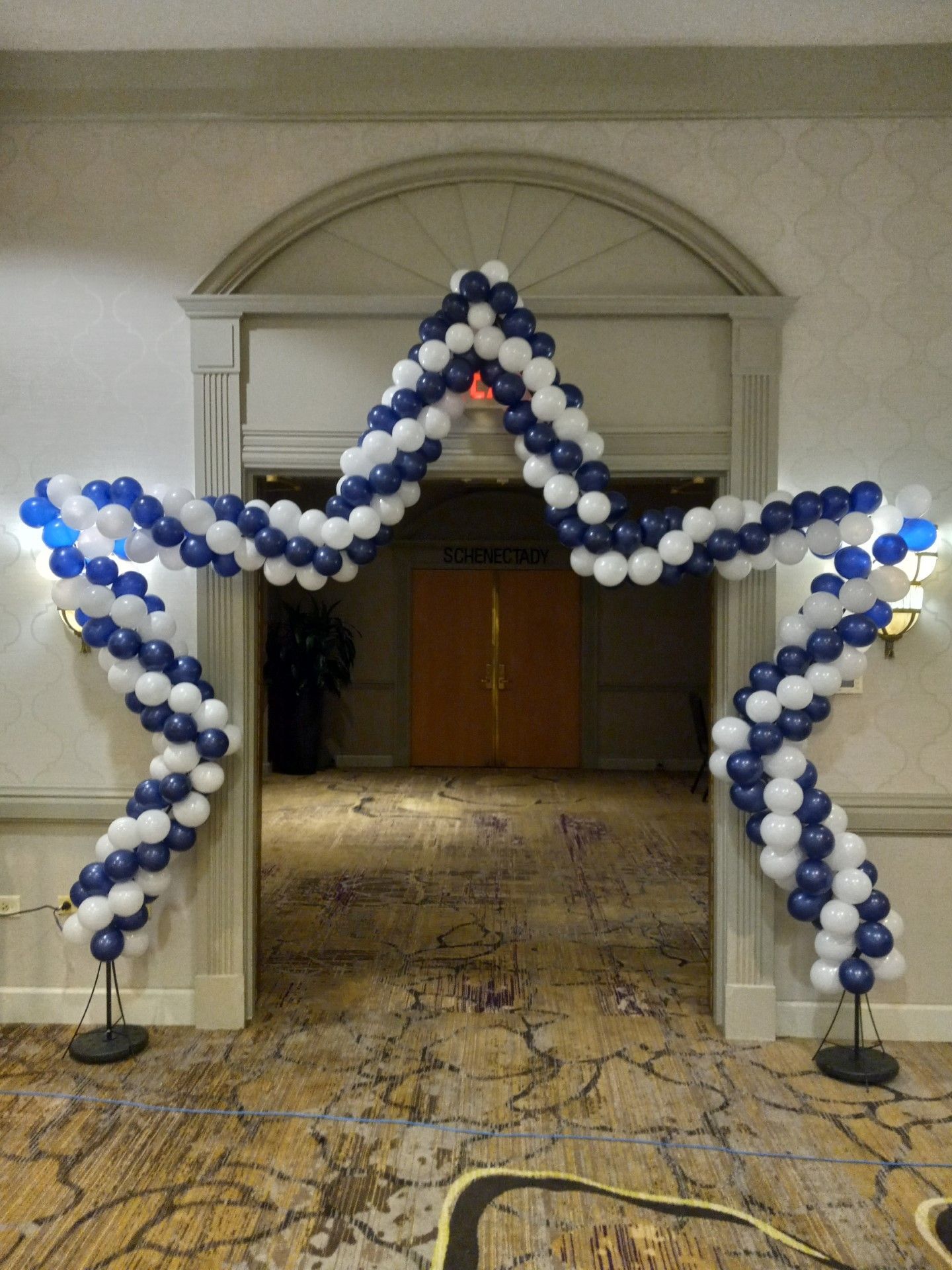 Star-shaped balloon arch in blue, white, and silver at a doorway in a decorated hallway