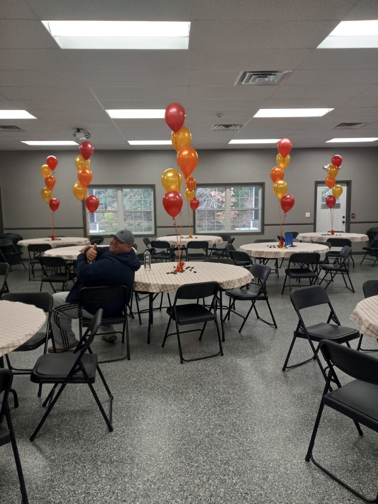 Conference room with round tables, folding chairs, and red and yellow balloon centerpieces.