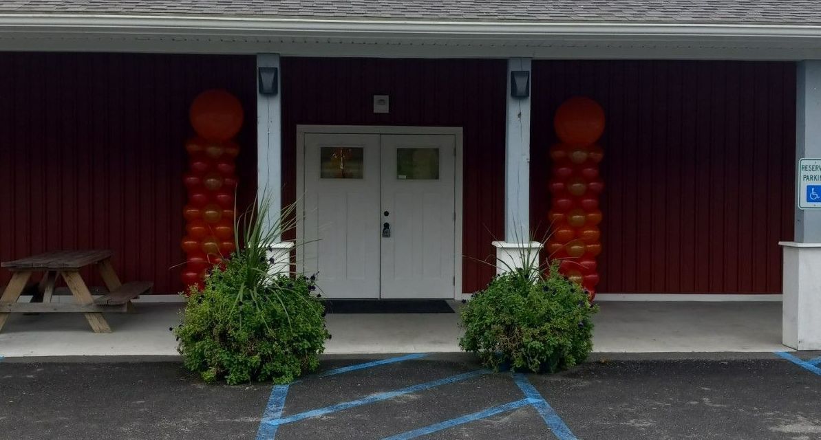 White double doors at a building entrance, framed by red columns and potted shrubs.