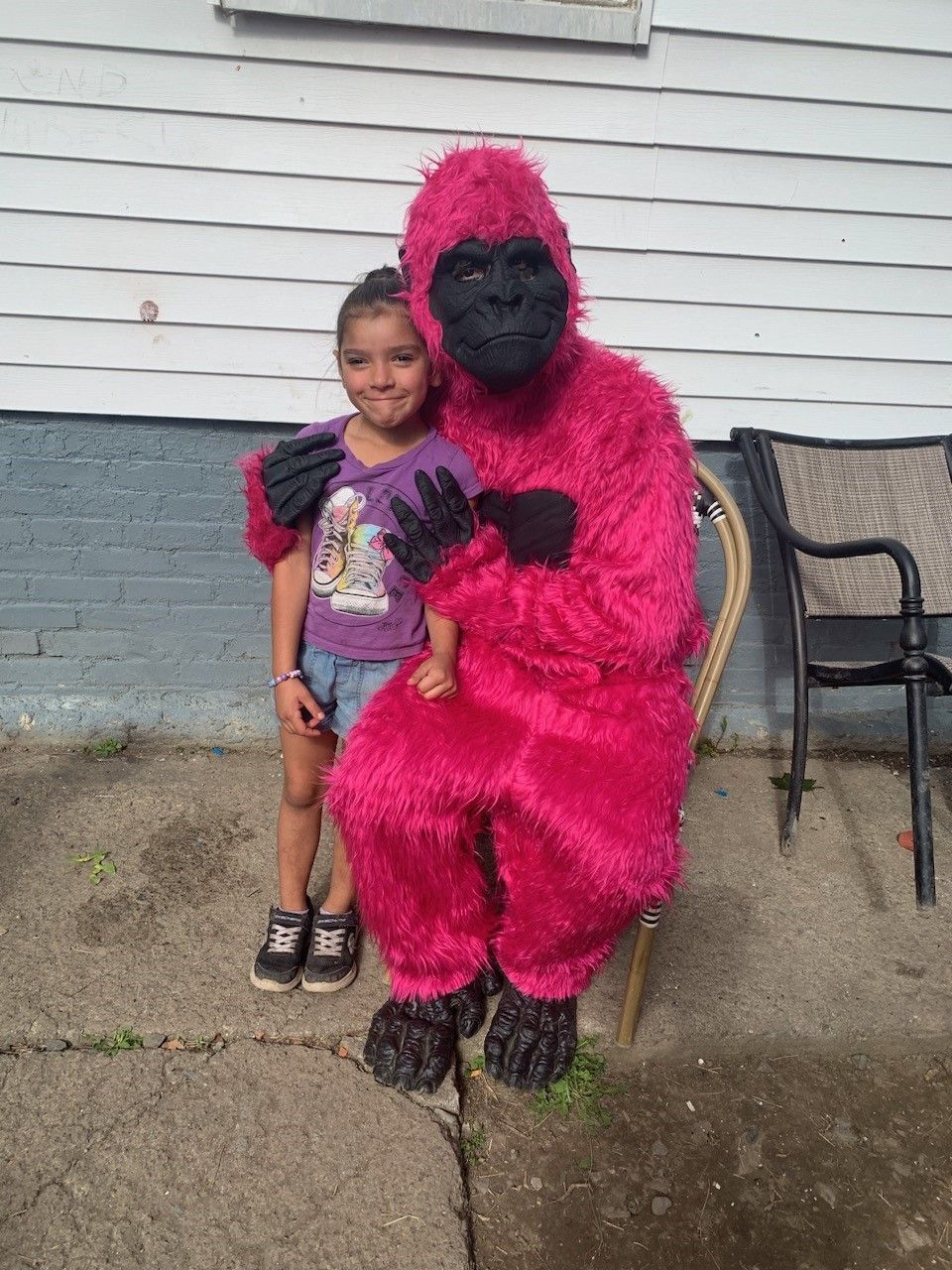Child posing with a person in a bright pink gorilla costume outside a house