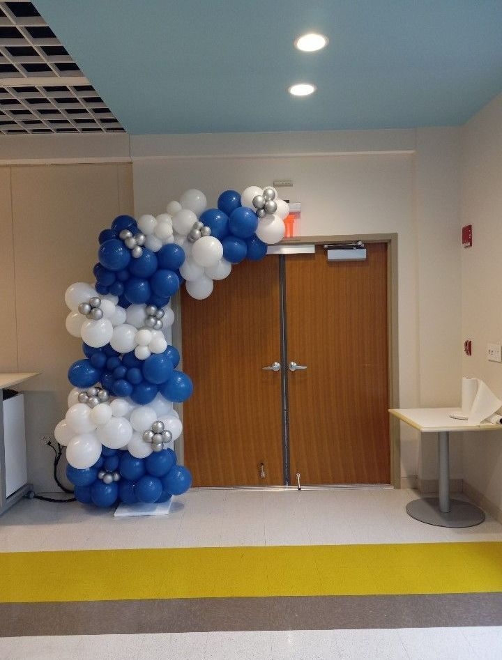 Blue and white balloon arch framing double wooden doors in a hallway