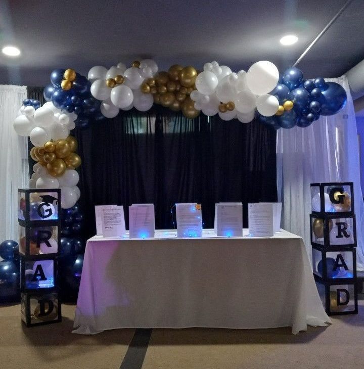 Graduation party backdrop with black, white, and gold balloons, a table, and “GRAD” columns