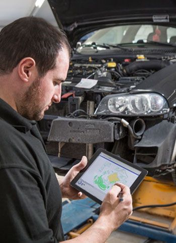 A man is looking at a tablet in front of a car.