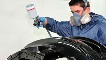 A man wearing a mask is spray painting a car bumper.