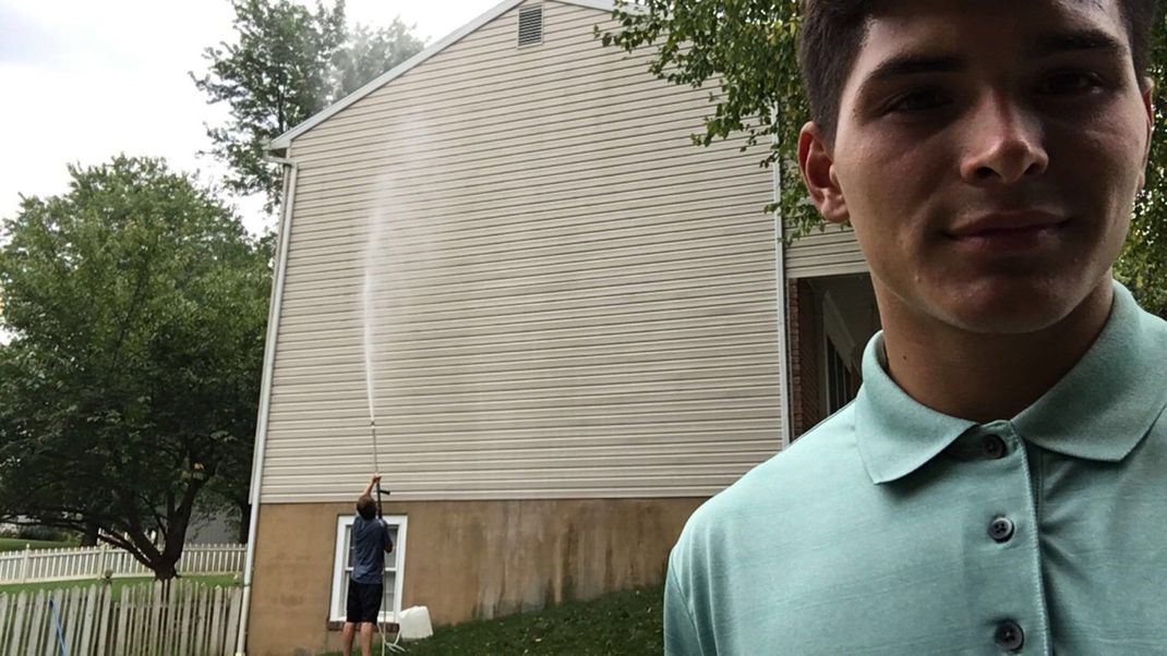 Soft washing a house in Mechanicsburg pa after image A man in a green shirt is standing in front of a house.