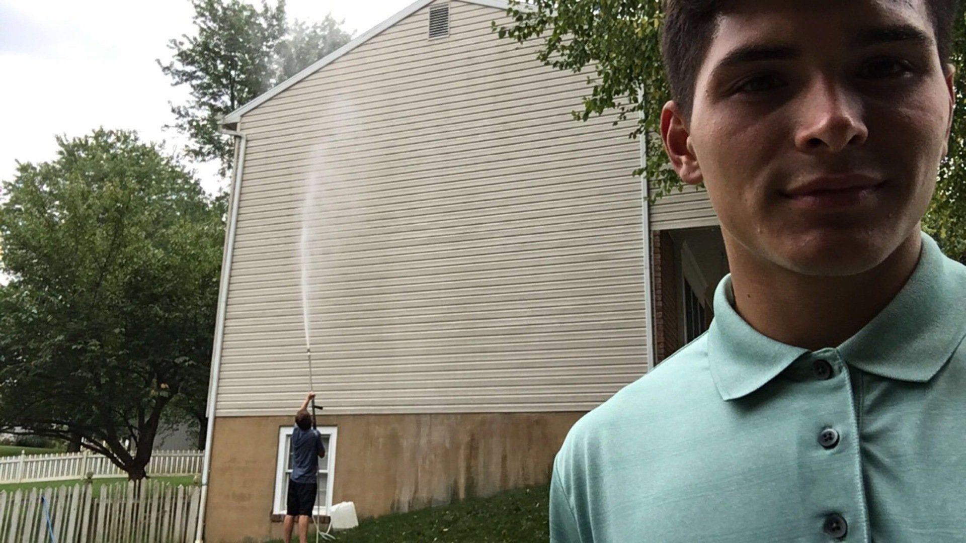 Soft washing a house in Mechanicsburg pa after image A man in a green shirt is standing in front of a house.