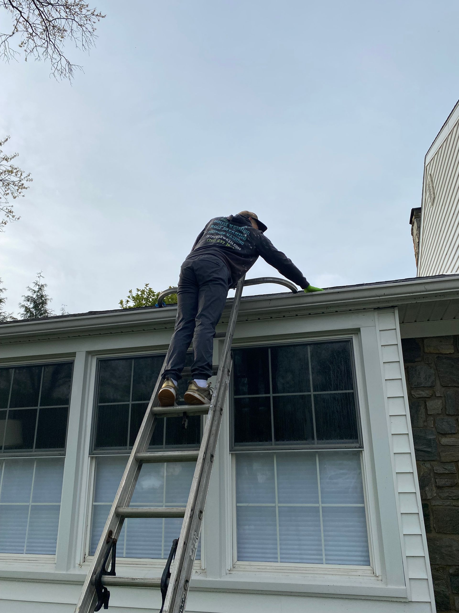 A man is standing on top of a roof with a gutter filled with leaves.