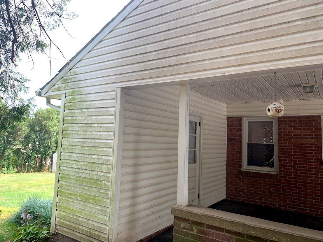 A house with a white siding and a brick wall has a porch.
