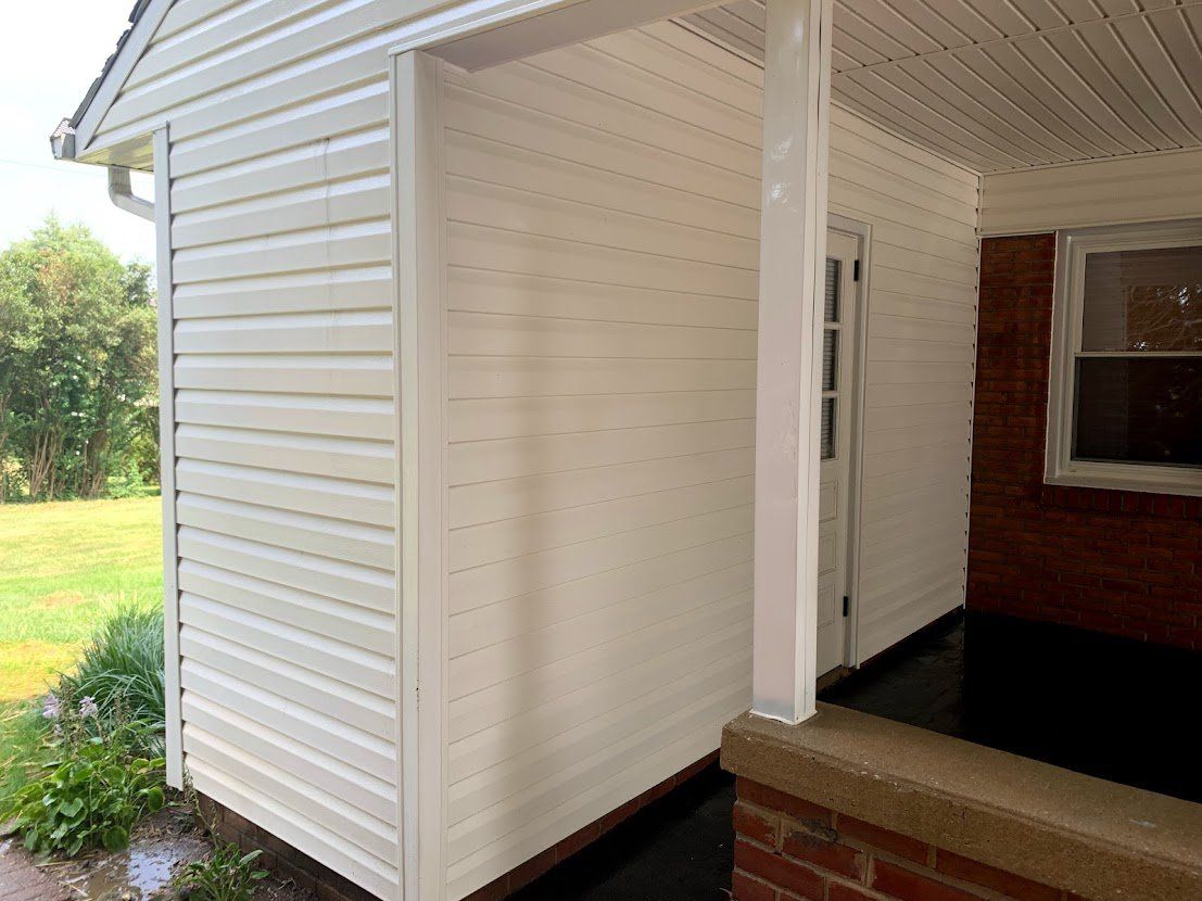 A white house with a porch and a brick wall.