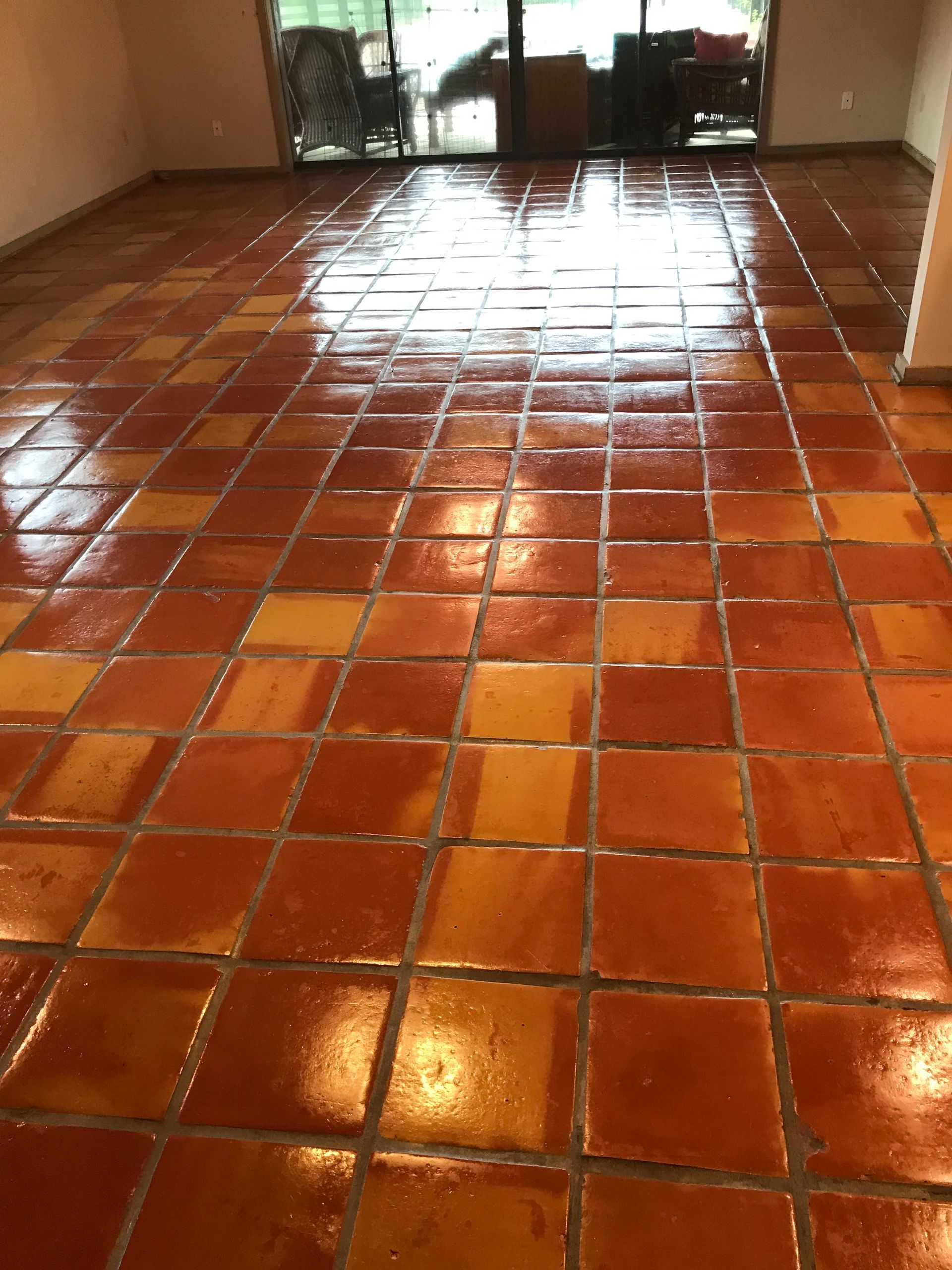 Red and orange tiled floor reflecting light, in a room with a sliding glass door to the outdoors.