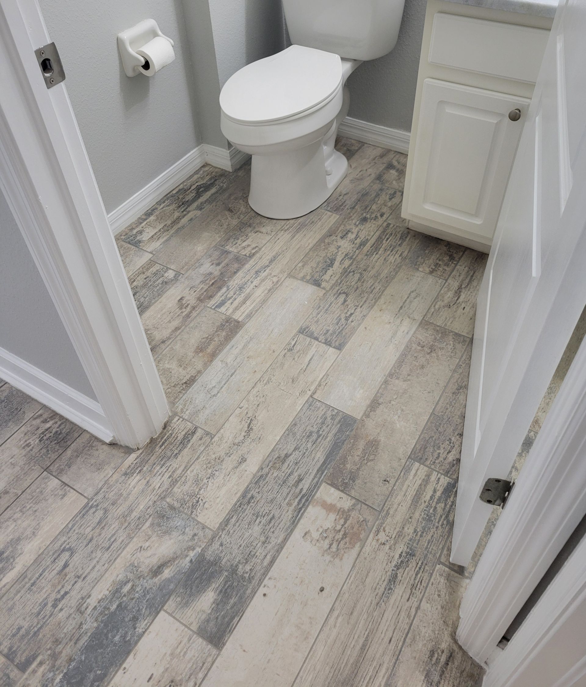 Bathroom with wood-look flooring, white toilet, cabinet, and door frames. Light gray walls.