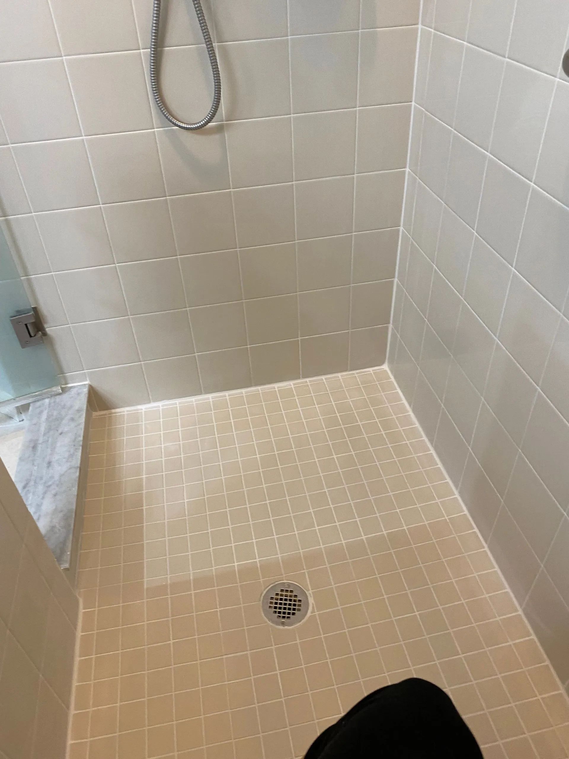 Empty beige tiled shower with a drain and handheld shower hose.