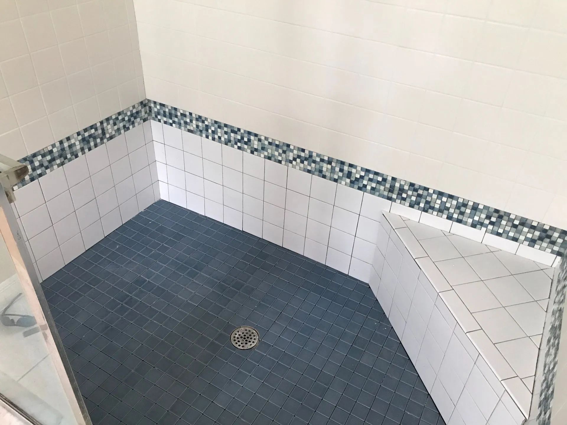 Empty tiled shower stall with blue floor tiles, white walls, and a small mosaic border