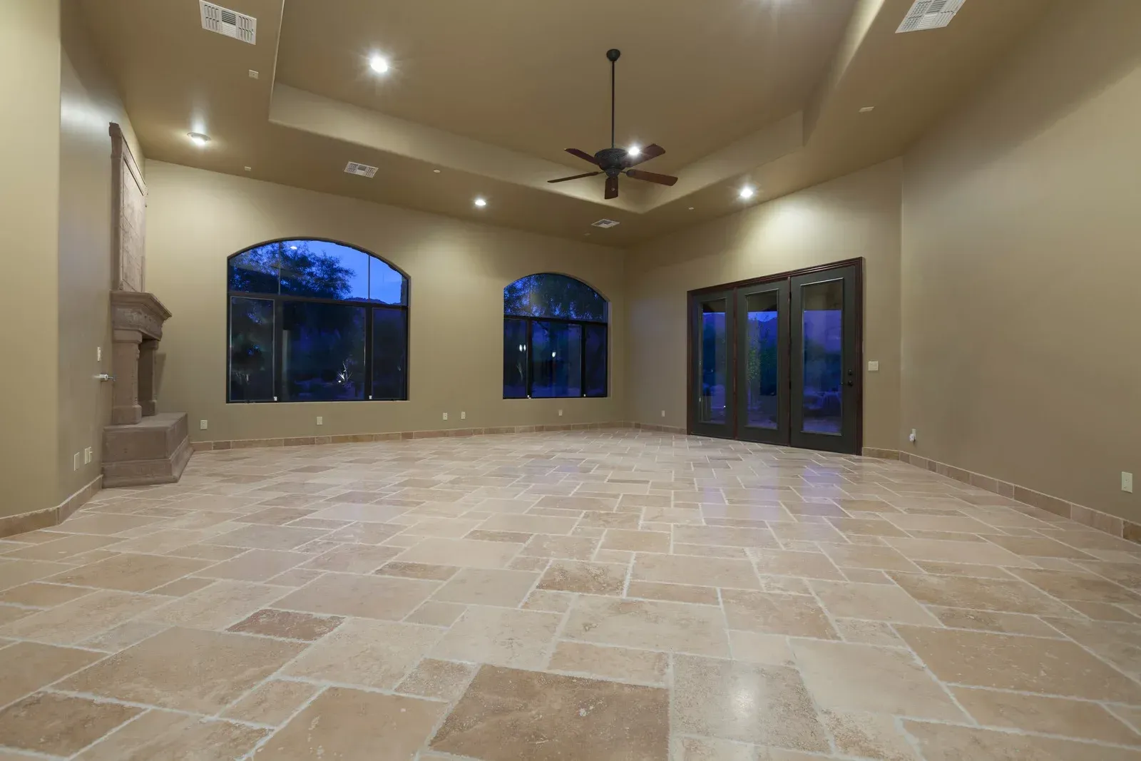Empty beige room with tile floor, arched windows, and a fireplace.
