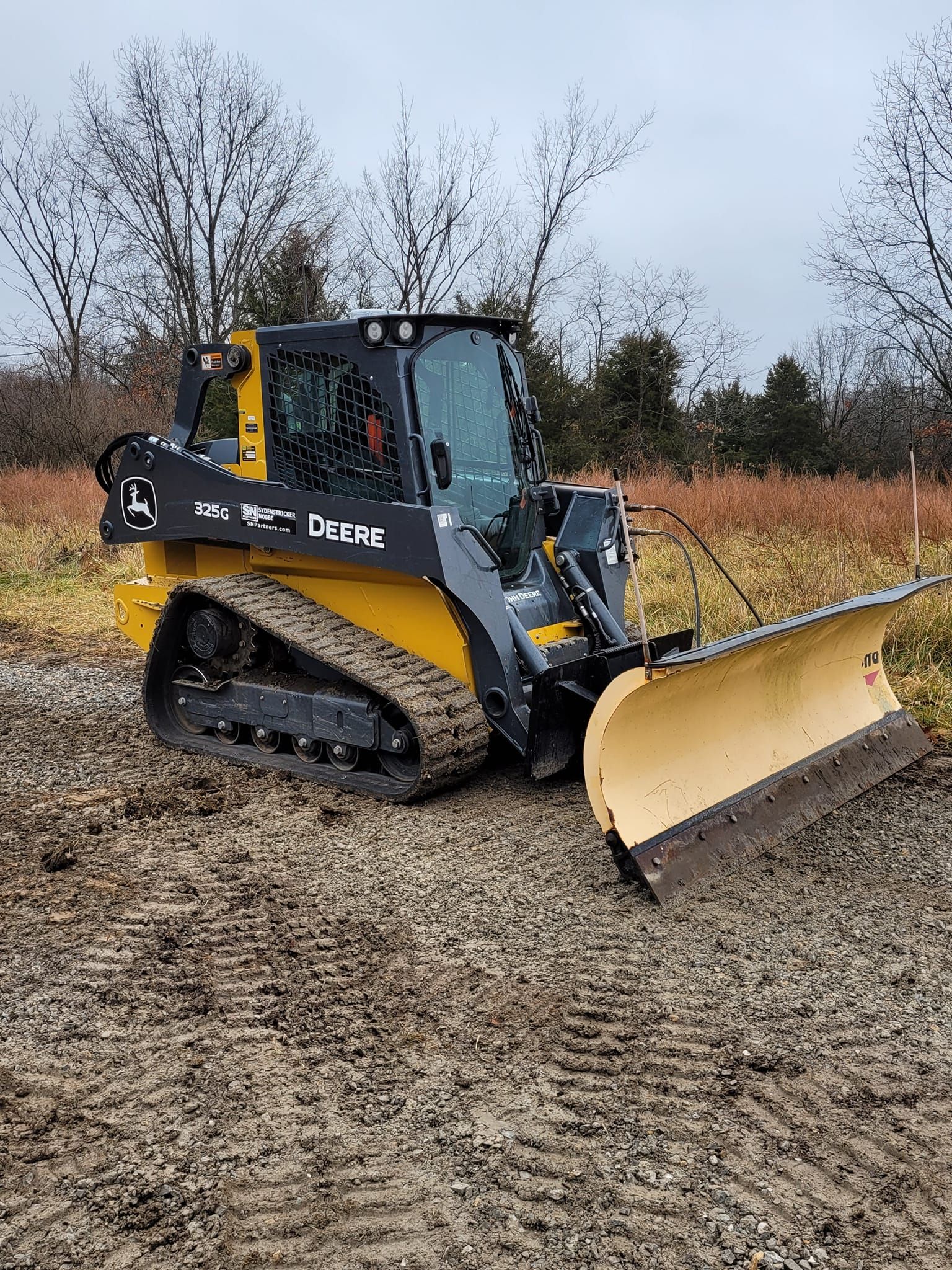 a yellow and black bulldozer with a snow plow attached to it is parked on a dirt road .