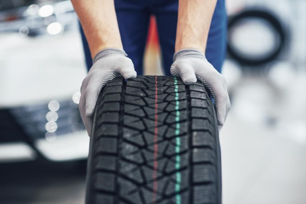 A Man Is Holding a Tire in His Hands in Front of A Car — Petersen's Second Hand & New Tyres in Currajong, QLD