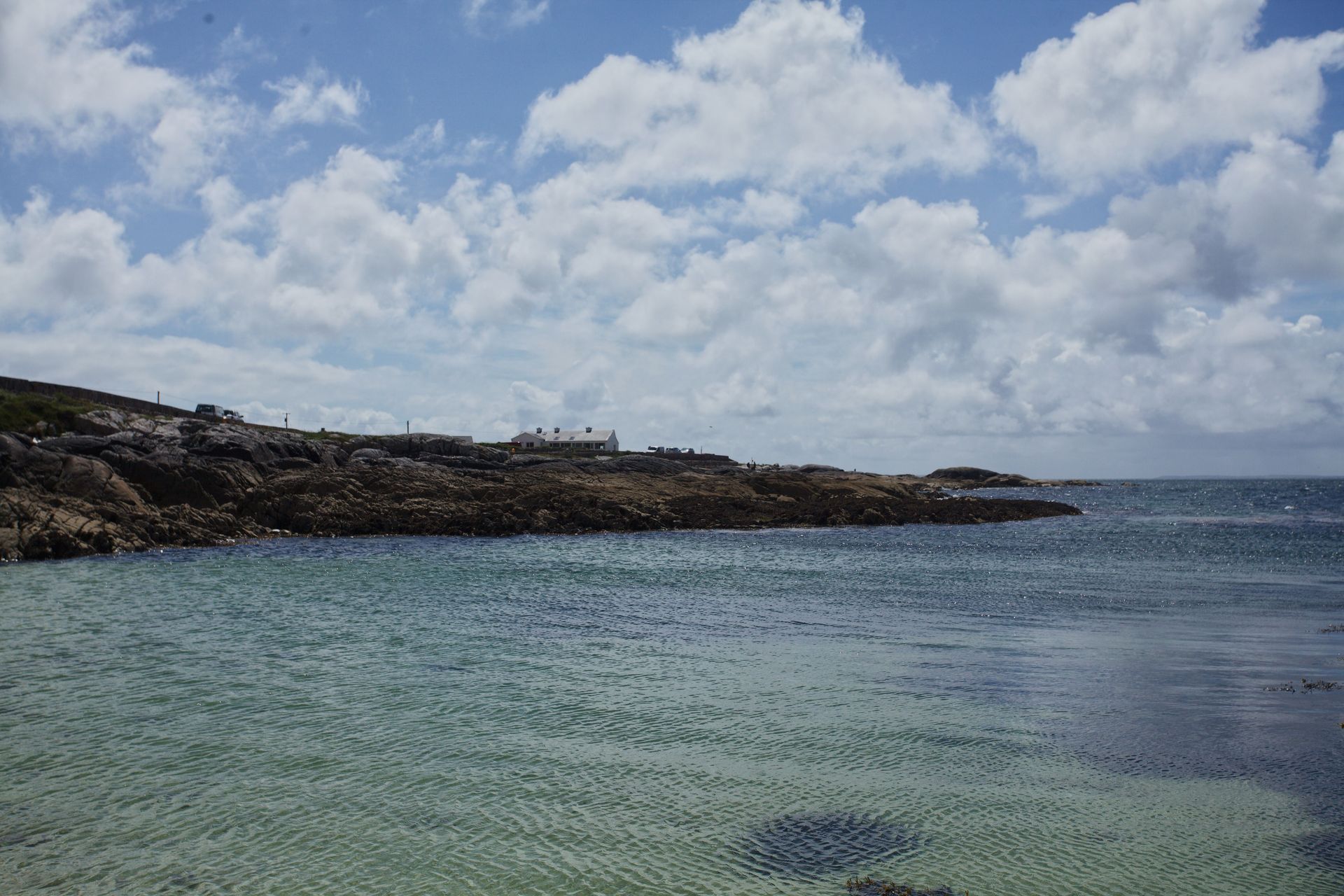 Rocky coastline beside clear blue water under a cloudy sky