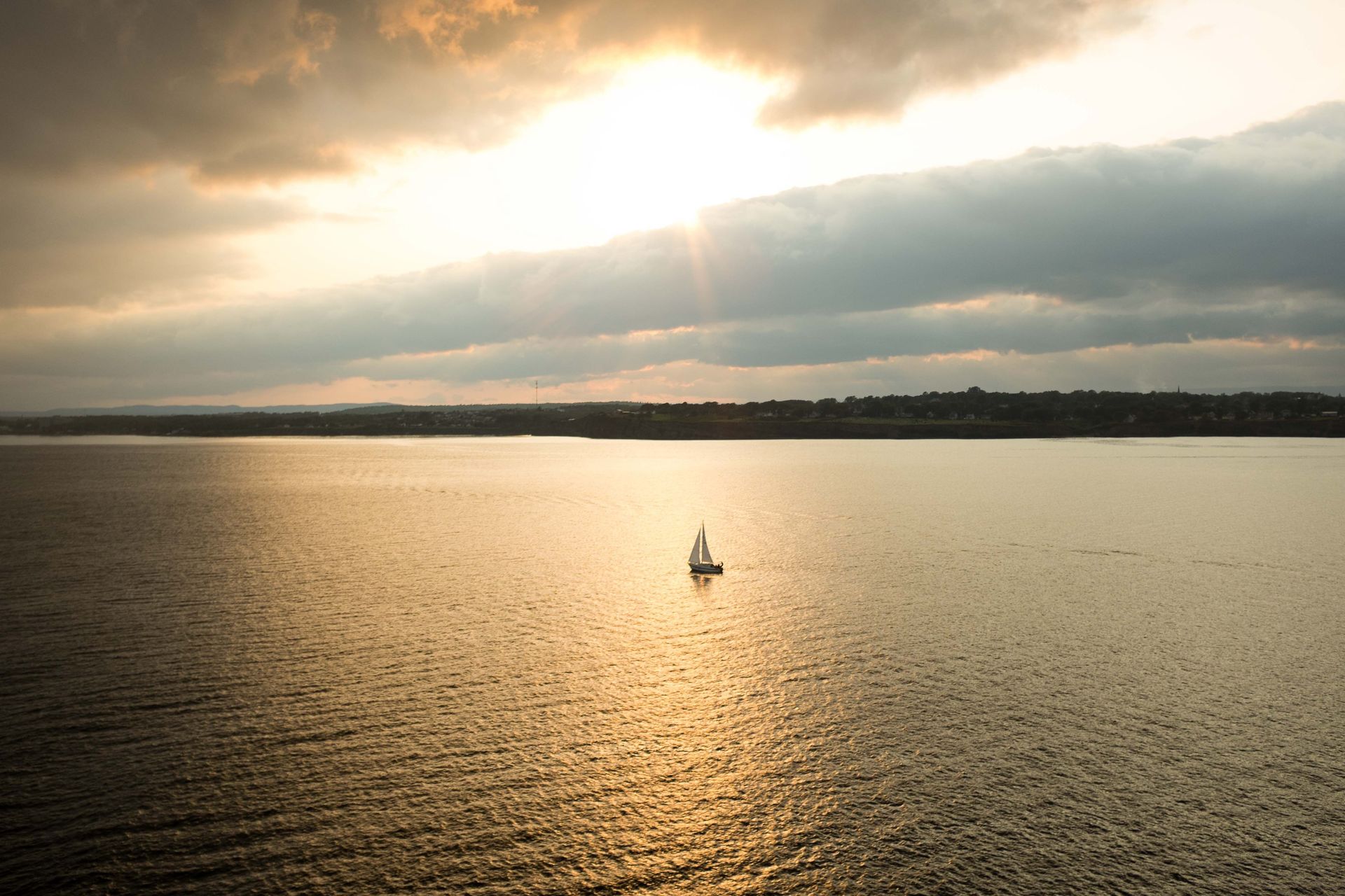 Small sailboat on a calm golden lake at sunset beneath cloudy skies.