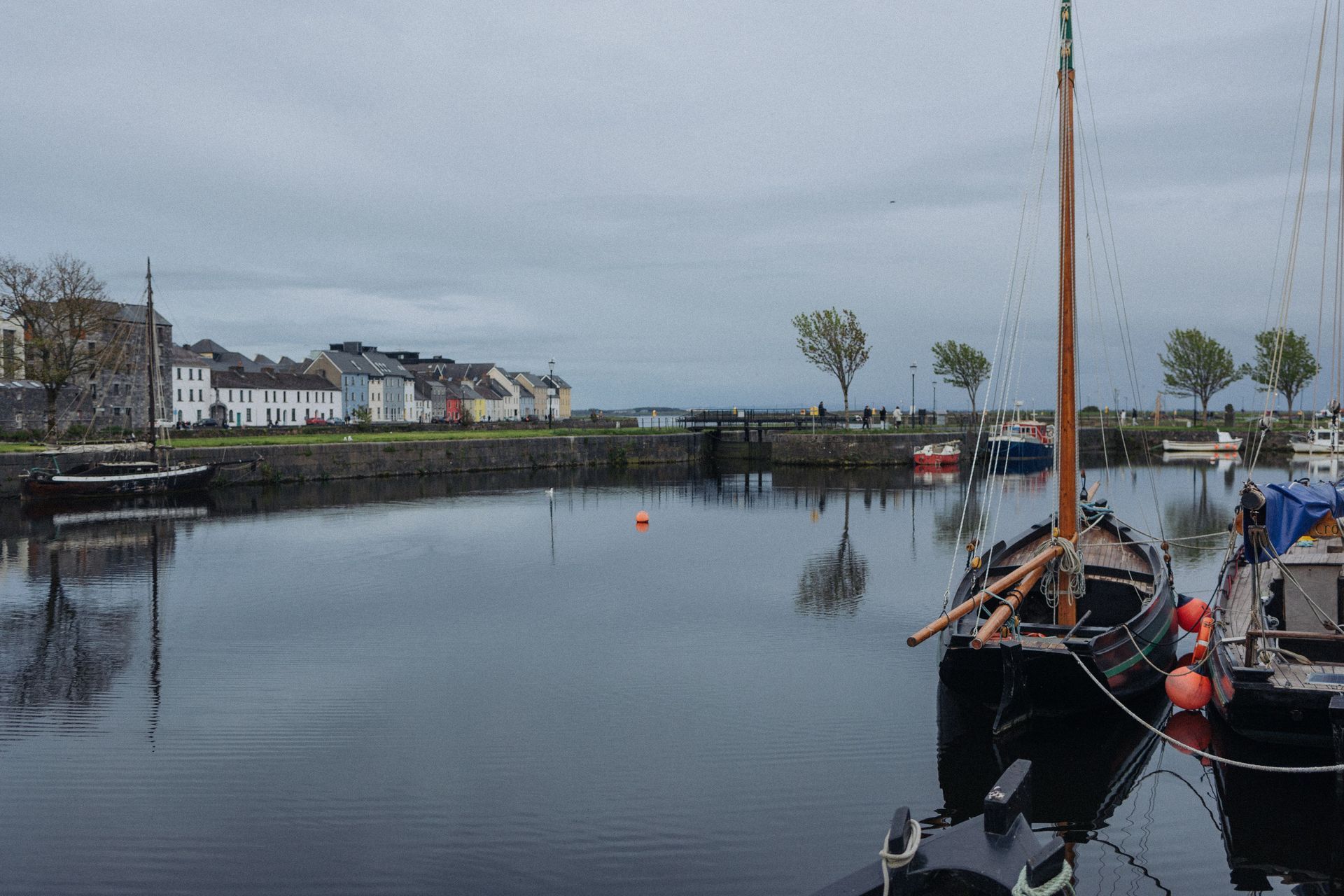 Calm harbor with docked boats, a waterfront row of houses, and overcast sky