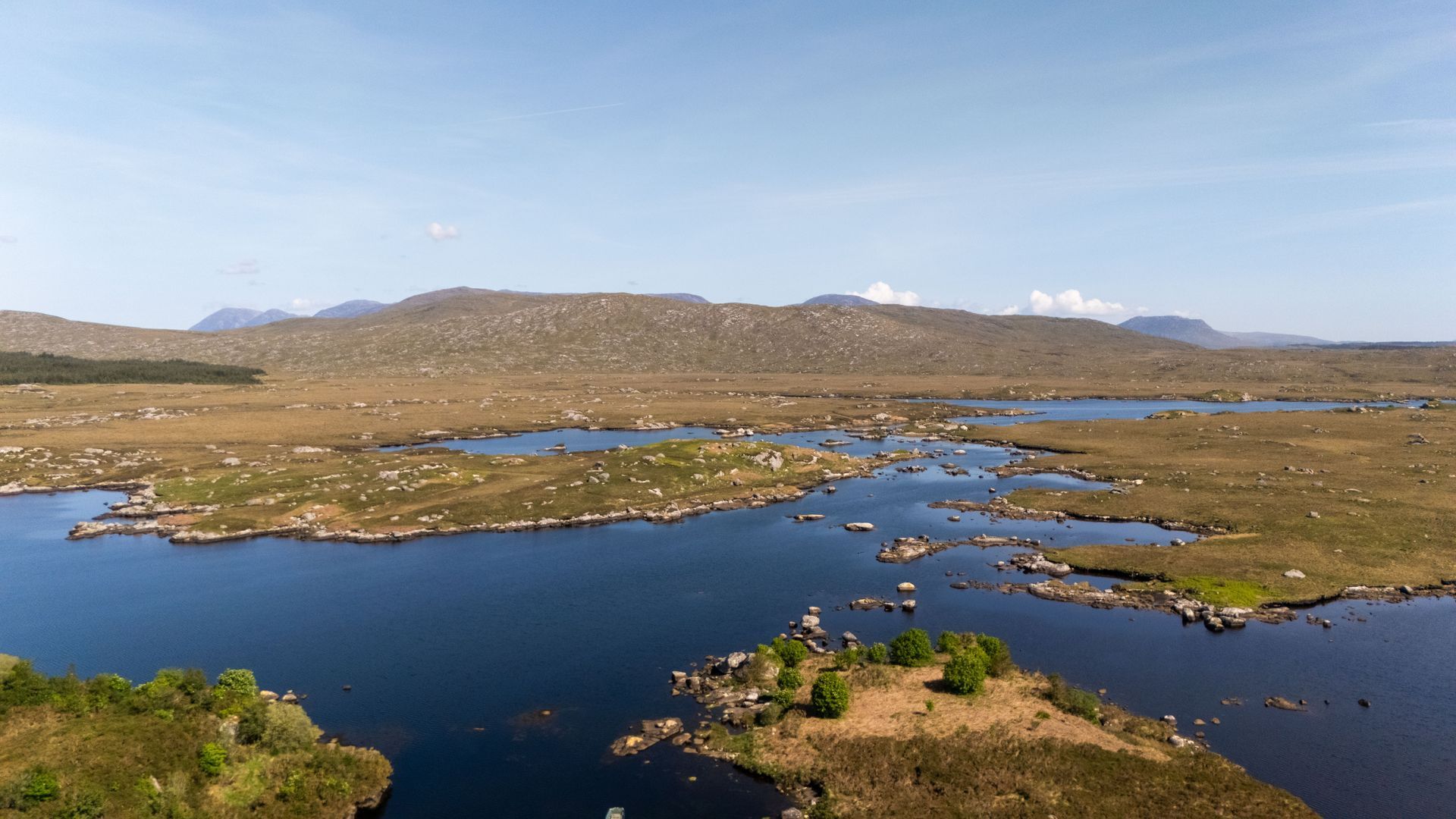 Wide blue lake with small islands in a grassy, mountainous landscape under a clear sky
