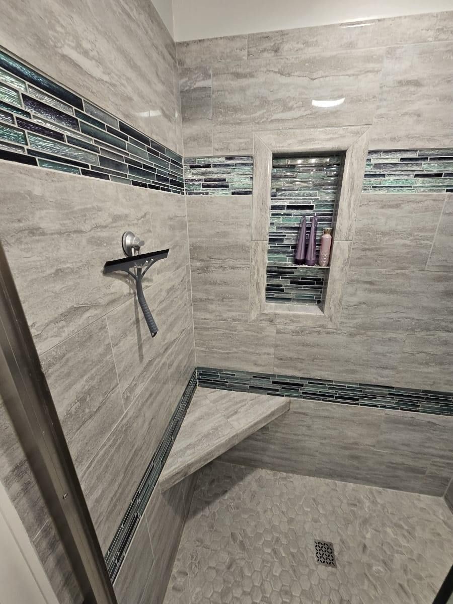 Gray and blue tiled shower with built-in bench, shelf, and glass shower door.