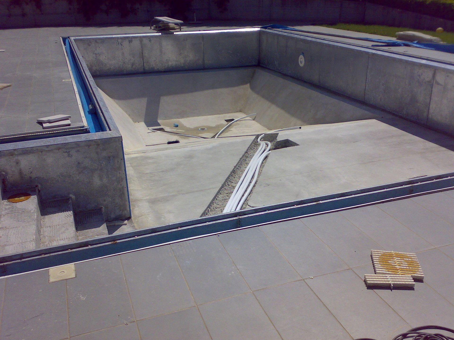 Piscina vuota in cemento in costruzione, con gradini e terrazza circostante.